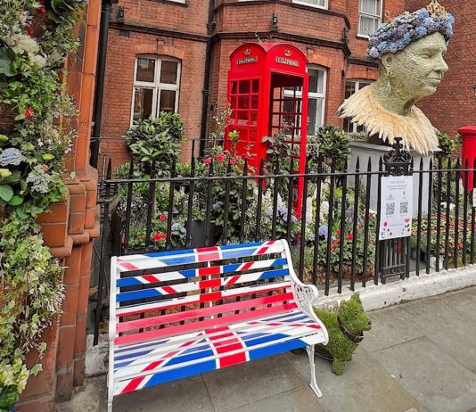 Angielski ogródek w którym znajduje się budka telefoniczna, skrzynka pocztowa, popiersie królowej Elżbiety i ławka pomalowana w brytyjską flagę